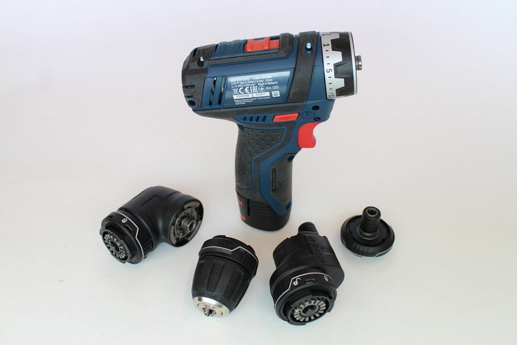 The compact Bosch drill driver, surrounded by its four interchangeable chucks and adaptors