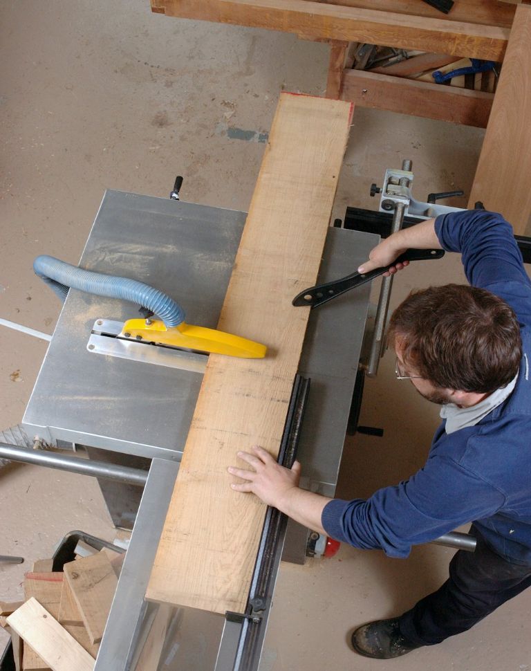 Seen from overhead, here, John Bullar is cross-cutting a board on the table saw’s sliding carriage, using a push-stick in his right hand